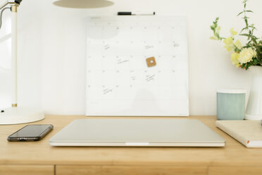 High angle view of laptop computer with mobile phone and calendar on wooden desk in office - CAVF60954