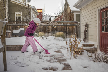 Seitenansicht eines Mädchens, das im Winter den Schnee im Hinterhof entfernt - CAVF60969