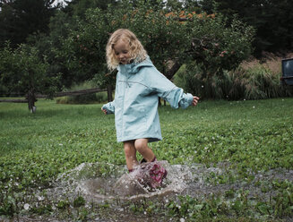 Verspieltes Mädchen spritzt Wasser in einer Pfütze im Apfelgarten - CAVF60994