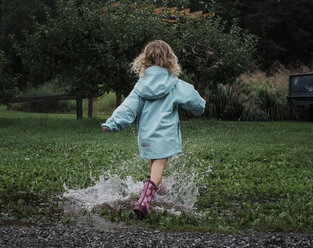 Rear view of playful girl splashing water in puddle at apple orchard - CAVF60995