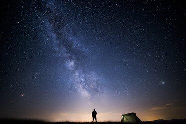 Rückansicht der Silhouette eines Mannes, der auf einem Feld vor einem Sternenfeld auf einem Campingplatz steht - CAVF61004