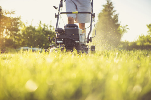 Midsection of man mowing grassy field against sky in yard during sunset stock photo