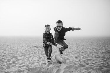 Verspielte Brüder springen auf Sand am Strand gegen den Himmel bei nebligem Wetter - CAVF61040