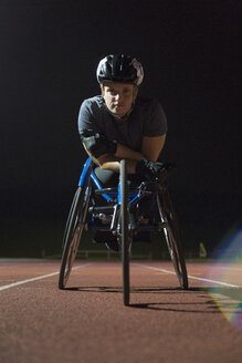 Porträt einer entschlossenen, zähen jungen querschnittsgelähmten Athletin, die nachts auf einer Sportbahn für ein Rollstuhlrennen trainiert - CAIF22617