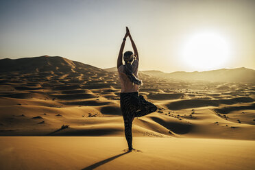 Serene woman standing in yoga tree pose in sunny sandy desert, Sahara, Morocco - CAIF22622