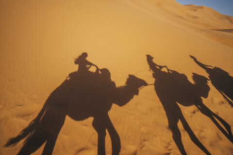 Schatten von Menschen reiten Kamele in sandigen Wüste, Sahara, Marokko, lizenzfreies Stockfoto