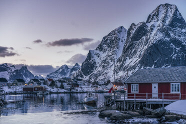 Tranquil fishing village below snowy mountains, Reine, Lofoten Islands, Norway - CAIF22630
