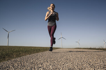 Junge Frau beim Joggen auf dem Feldweg, Windräder im Hintergrund - SEBF00003
