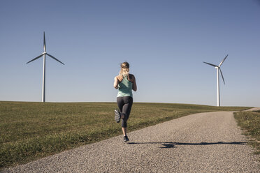 Junge Frau beim Joggen auf dem Feldweg, Windräder im Hintergrund - SEBF00004