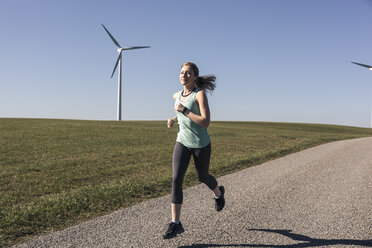 Junge Frau beim Joggen auf dem Feldweg, Windräder im Hintergrund - SEBF00007