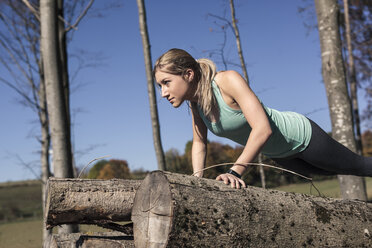 Junge Frau macht Liegestütze auf einem Baumstamm beim Training in der Natur - SEBF00008