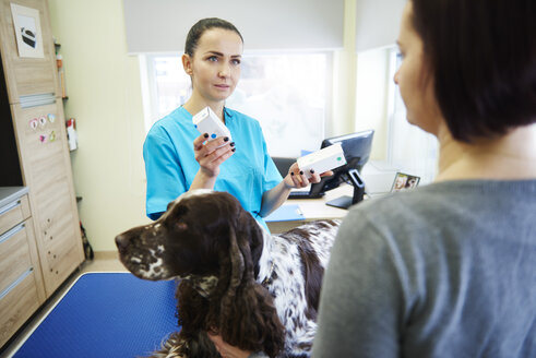 Tierärztin, die einem Hundebesitzer in einer Tierarztpraxis Medikamente verabreicht - ABIF01228