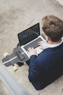 Junger Geschäftsmann mit Skateboard sitzt im Freien auf einer Treppe und benutzt einen Laptop - MOEF02072