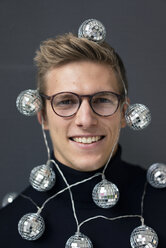 Porträt eines lächelnden jungen Mannes mit Spiegelkugel-Lichterkette - MOEF02074