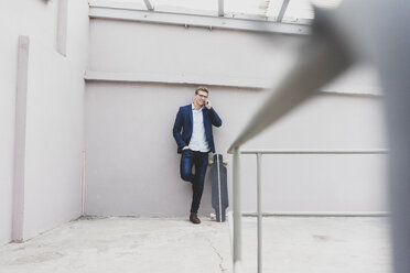 Smiling young businessman with skateboard leaning against a concrete wall talking on cell phone - MOEF02079