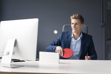 Young businessman sitting at desk in office playing table tennis - MOEF02092