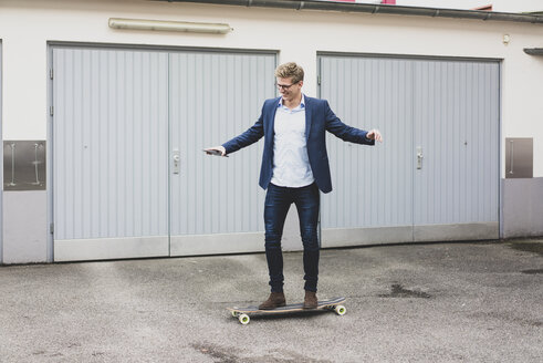 Junger Geschäftsmann fährt Skateboard vor dem Garagentor - MOEF02102