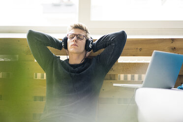 Relaxed young man sitting on the floor listening to music with headphones - MOEF02116