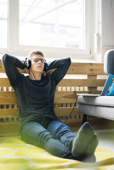 Relaxed young man sitting on the floor listening to music with headphones - MOEF02119