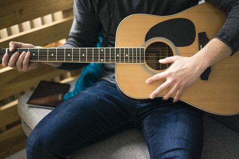 Nahaufnahme eines Mannes, der auf einer Couch sitzt und Gitarre spielt, lizenzfreies Stockfoto