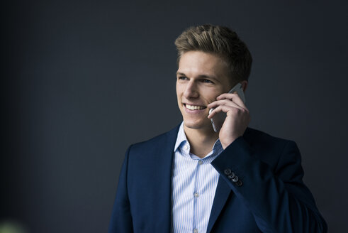 Porträt eines lächelnden jungen Geschäftsmannes am Mobiltelefon - MOEF02156