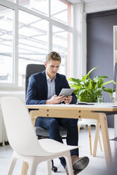 Selbstbewusster junger Geschäftsmann sitzt am Schreibtisch im Büro und benutzt ein Tablet - MOEF02164