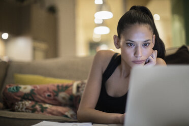 Fokussierte Frau im Pyjama mit Laptop auf dem Sofa - CAIF22661