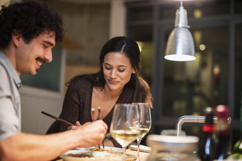 Ehepaar isst mit Stäbchen und trinkt Weißwein in der Wohnküche - CAIF22662