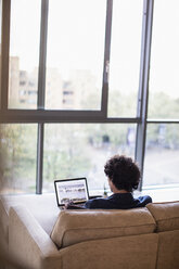 Mann mit Laptop auf dem Sofa einer städtischen Wohnung - CAIF22680