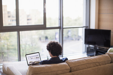 Mann mit Laptop auf dem Sofa in der Wohnung - CAIF22686