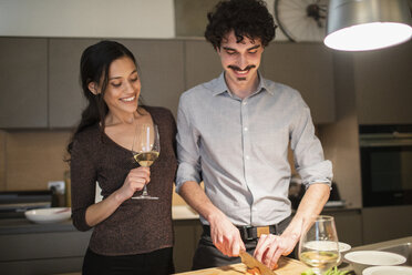 Glückliches Paar bei der Zubereitung des Abendessens und beim Trinken von Weißwein in der Wohnküche - CAIF22697
