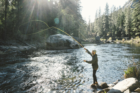 Seitenansicht eines Mannes beim Fliegenfischen auf einem Felsen im Fluss im Yosemite National Park - CAVF61062