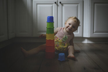 Portrait of cute baby girl with colorful toys while sitting on hardwood floor at home - CAVF61069