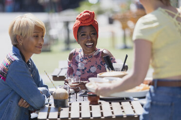 Young women friends enjoying lunch at sunny sidewalk cafe - CAIF22708