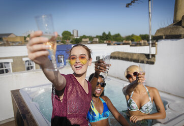Porträt zuversichtlich, sorglos junge Frauen Freunde trinken Champagner in sonnigen Dachterrasse Whirlpool - CAIF22720