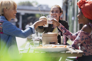 Junge Freundinnen stoßen mit Wassergläsern beim Dim Sum-Mittagessen in einem sonnigen Straßencafé an - CAIF22733
