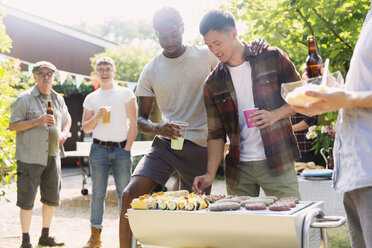 Männliche Freunde beim Grillen im sonnigen Sommergarten - CAIF22745