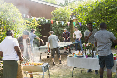 Männliche Freunde spielen Tischtennis und genießen das Grillen im Hinterhof - CAIF22747