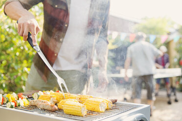 Man barbecuing corn, sausage and vegetable kebabs - CAIF22749