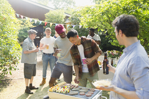 Männliche Freunde trinken Bier und grillen im sonnigen Sommergarten, lizenzfreies Stockfoto
