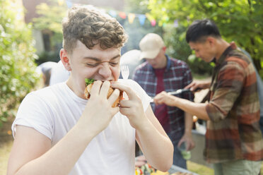 Hungriger Teenager isst Hamburger beim Grillen im Hinterhof - CAIF22753