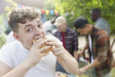 Portrait hungry teenage boy eating hamburger at backyard barbecue - CAIF22754