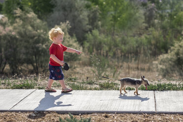Seitenansicht der niedlichen Baby-Junge zeigt, während zu Fuß mit Welpen auf Gehweg im Park - CAVF61091