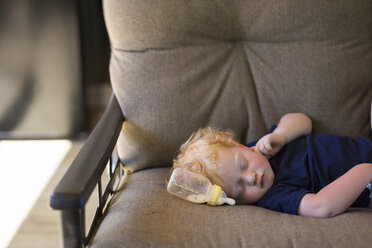 Niedliches Baby schlafend durch Milchflasche auf Couch zu Hause - CAVF61092