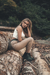 Seitenansicht des Porträts einer selbstbewussten Frau, die auf einem Baumstamm im Wald sitzt - CAVF61102