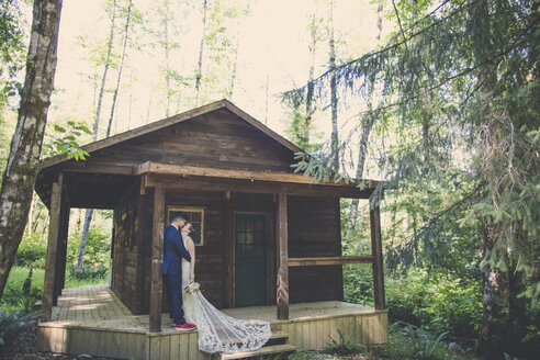 Ein frisch verheiratetes Paar küsst sich auf einer Veranda im Wald - CAVF61121