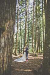 Side view of romantic newlywed couple embracing while standing amidst trees in forest - CAVF61122