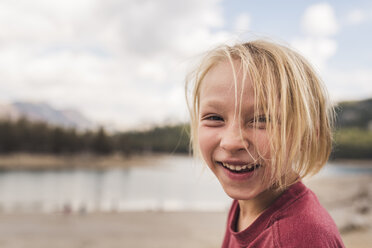 Porträt eines glücklichen Jungen mit blondem Haar vor einem bewölkten Himmel im Wald - CAVF61130
