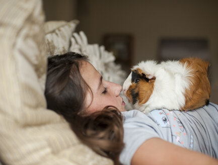 Seitenansicht eines Mädchens mit Meerschweinchen, das zu Hause auf dem Bett liegt - CAVF61133