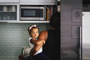 Rückansicht der Mutter, die ihre niedliche Tochter in der Küche zu Hause trägt - CAVF61141